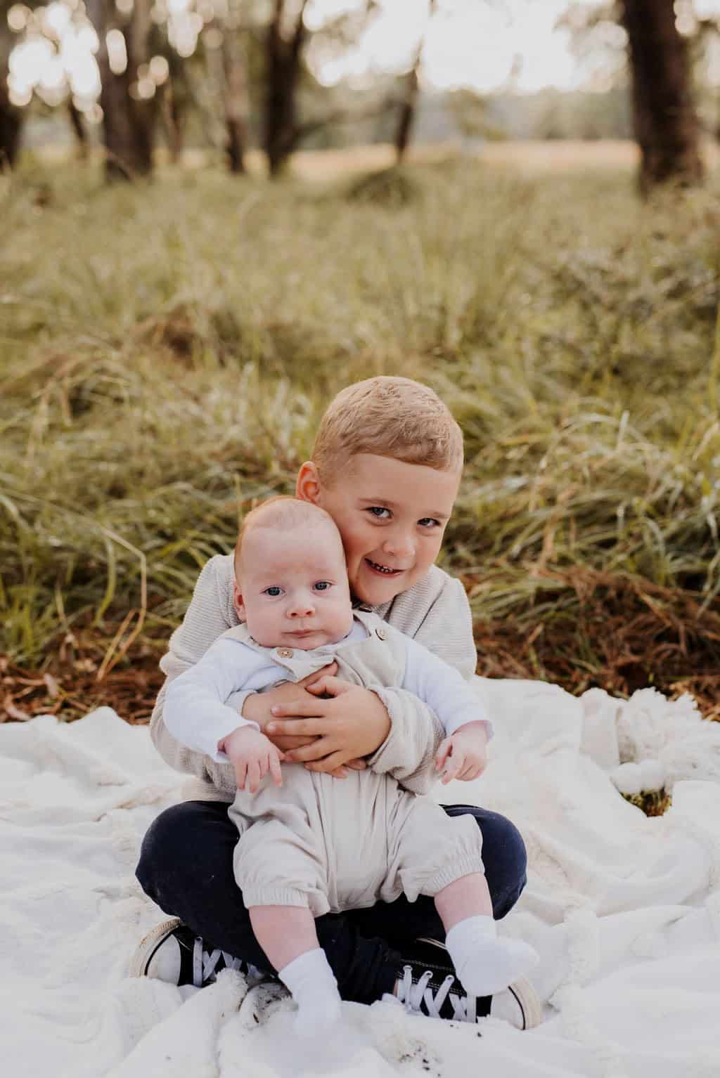 Baby with sagittal synostosis held by older brother outdoors