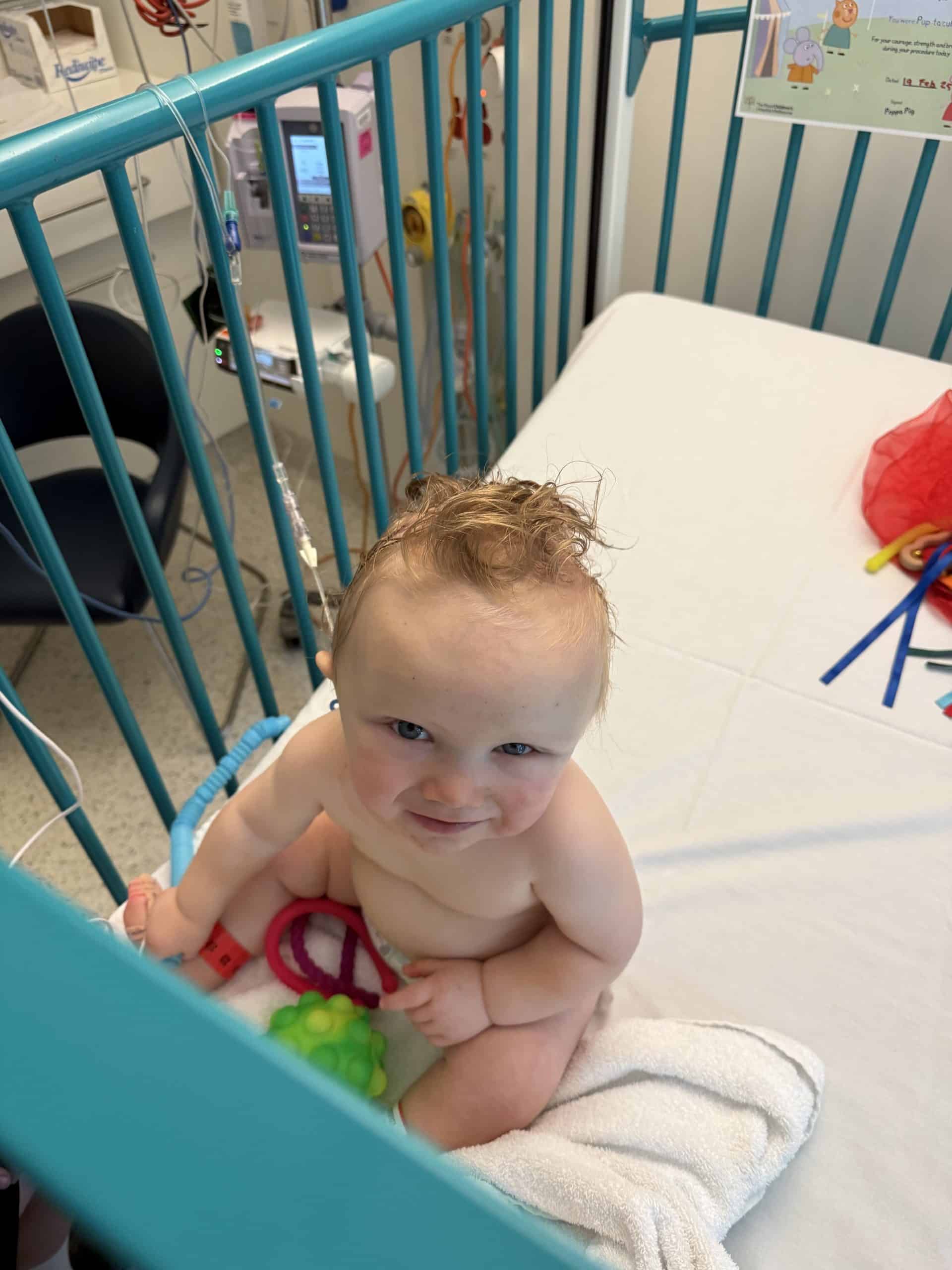 Baby with sagittal synostosis in hospital bed with medical equipment, following surgery.