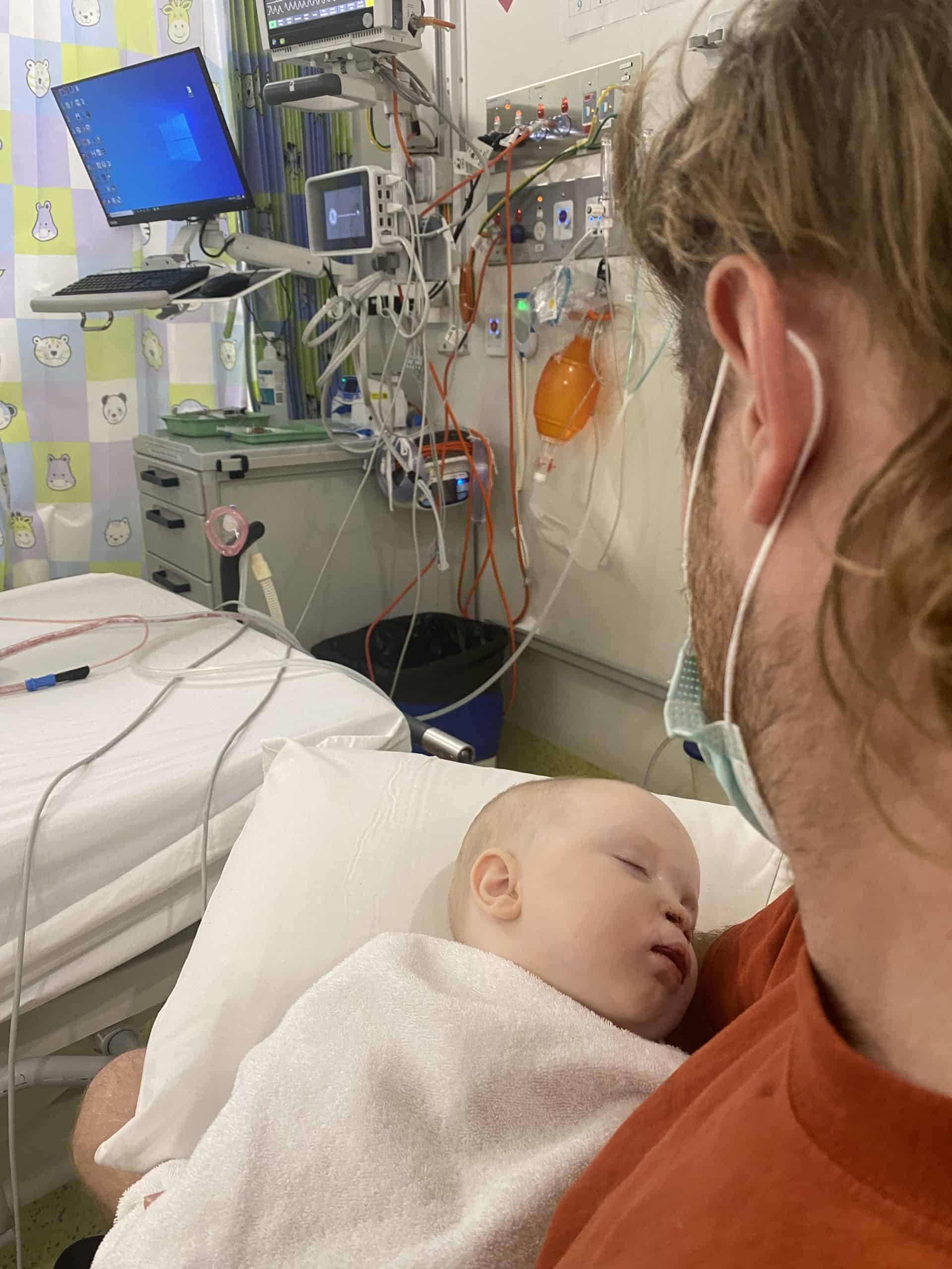Baby with cleft lip and palate held by father in a hospital room