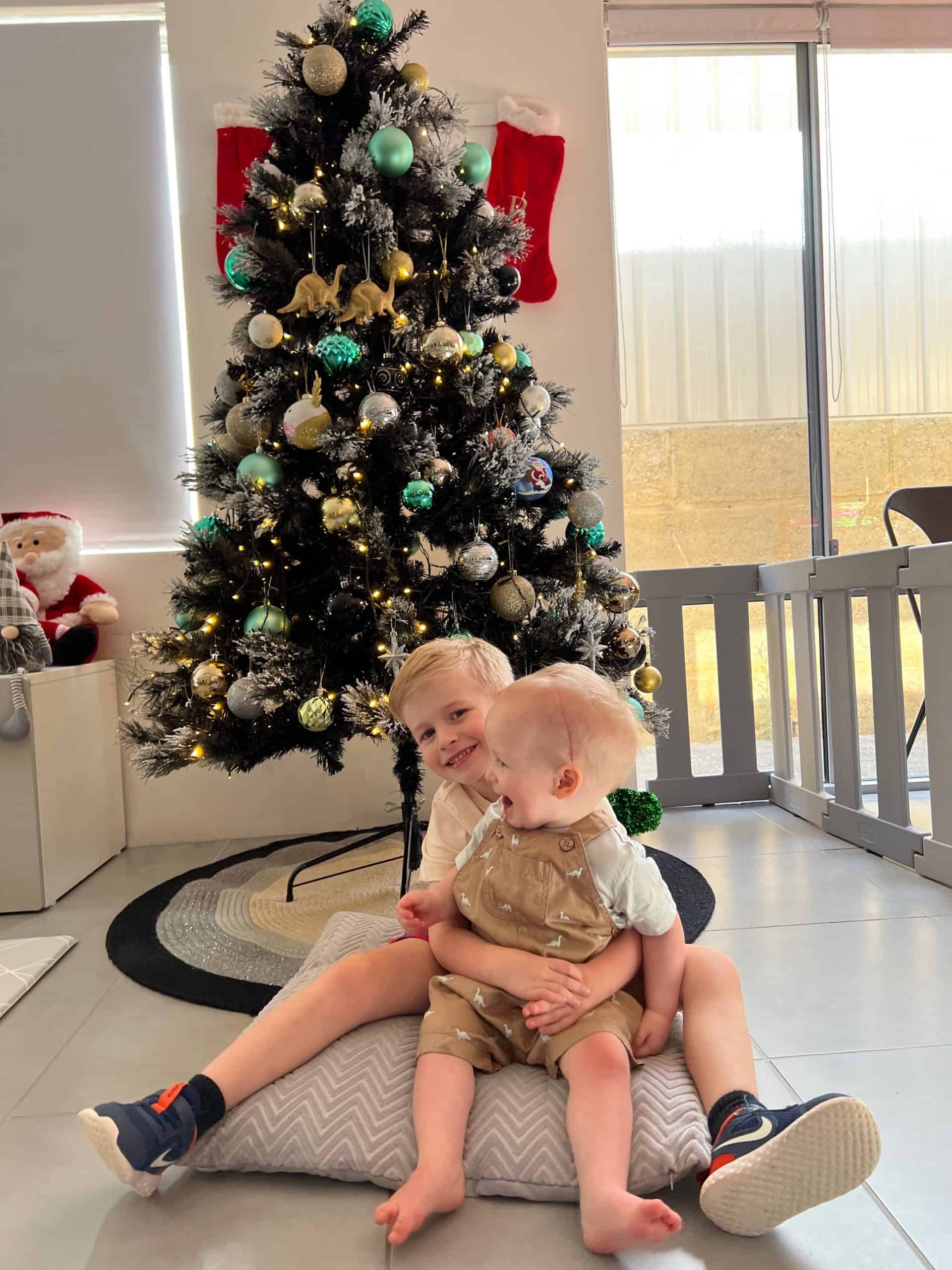 Baby boy with sagittal synostosis post surgery held by sibling sitting in front of a Christmas tree