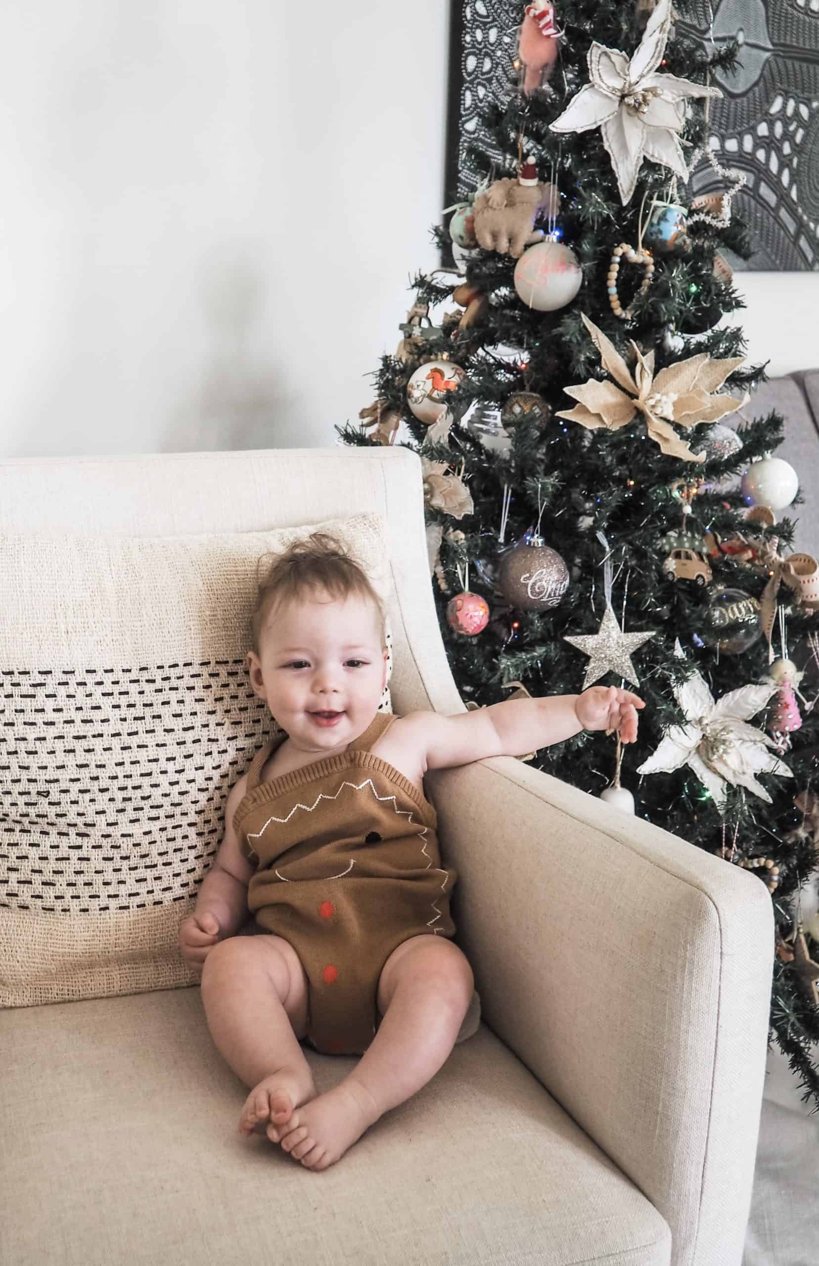 Baby with sagittal synostosis post-surgery sitting on a sofa with a Christmas tree behind