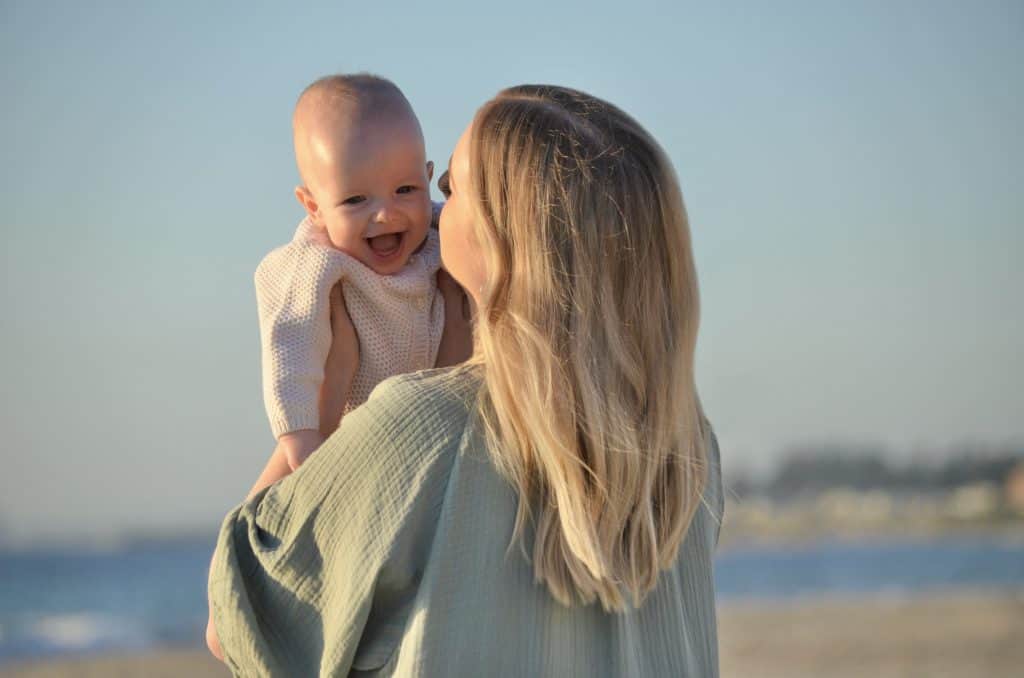 Baby boy with sagittal synostosis held by mother at the beach