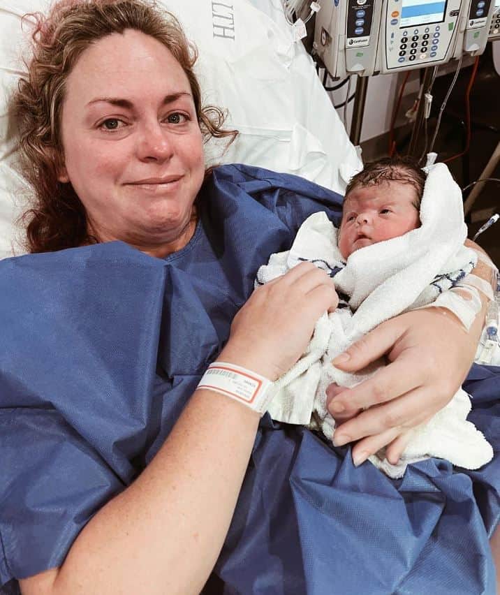 Baby girl with Apert syndrome held by mother, lying in hospital bed.