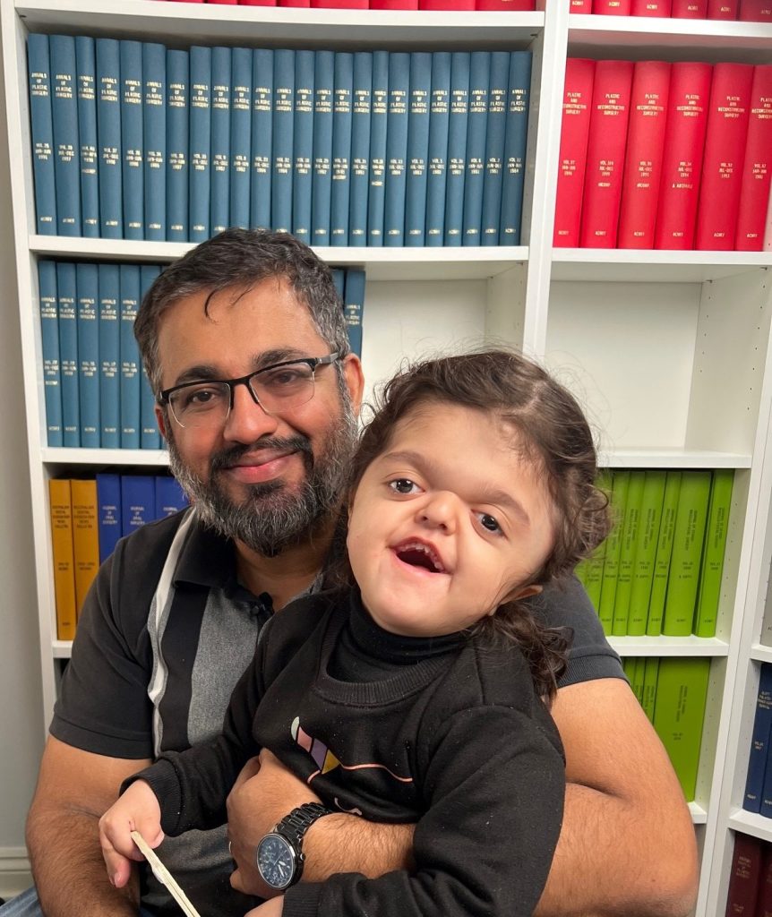 Father from Pakistan holding daughter who has Apert syndrome, sitting in the board room at Craniofacial Australia office