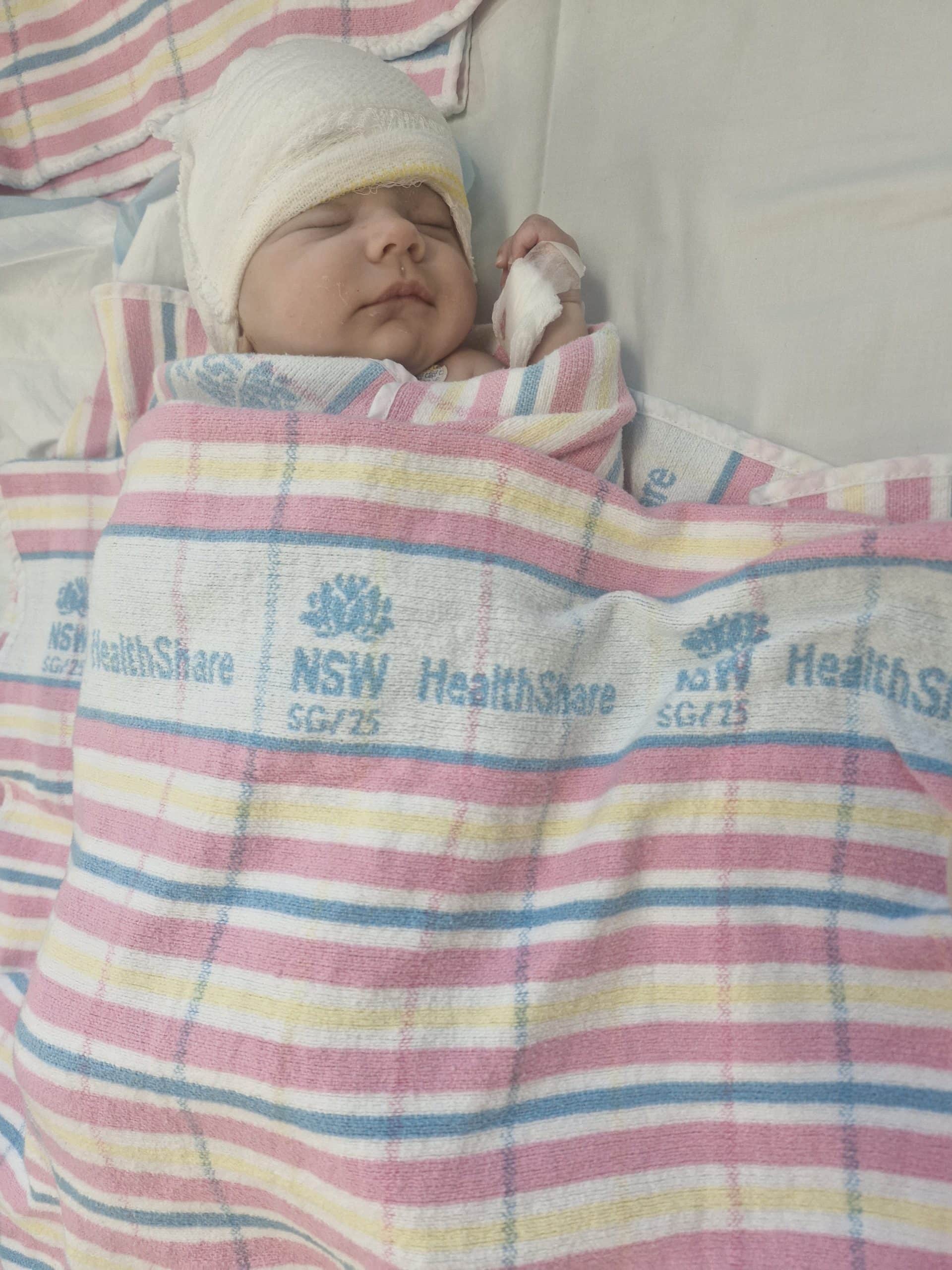Newborn baby in hospital bed wrapped in a striped blanket with a white cap.