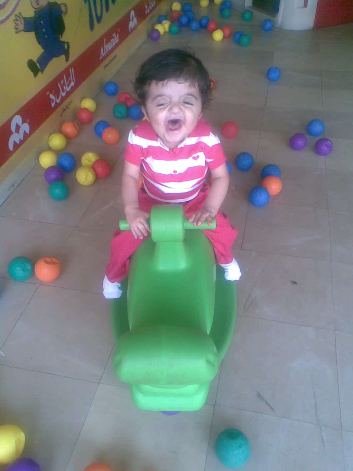 Child smiling on a green toy in a colourful play area at Craniofacial Australia.